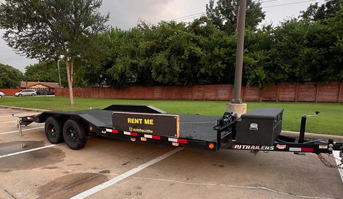 Black PJ flatbed trailer with toolbox parked in an outdoor lot