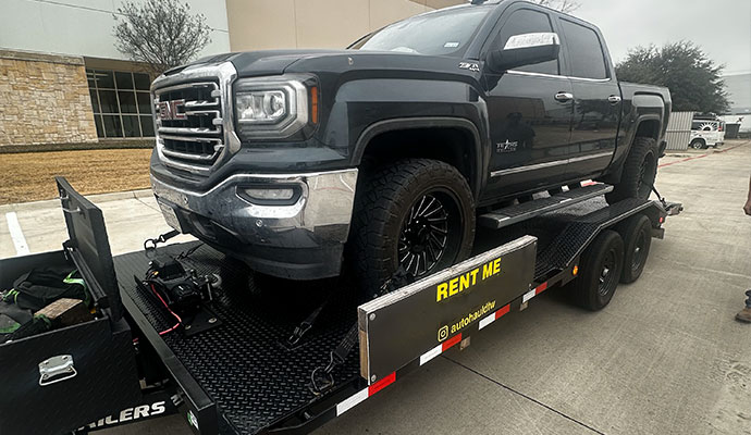 PJ Car Hauler trailer rented with winch, straps, and ramps, securely transporting a dark gray GMC Sierra pickup truck.
