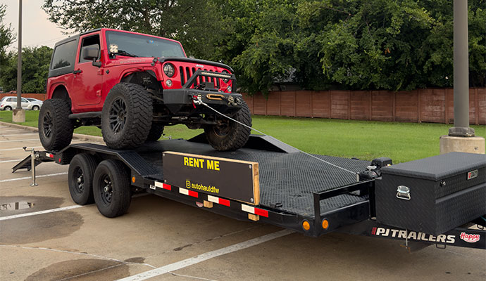 Red lifted Jeep Wrangler being securely hauled on a black PJ car hauler trailer.