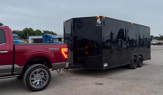 A black enclosed trailer hitched to a pickup truck, providing secure and weather-protected transport for vehicles or cargo.