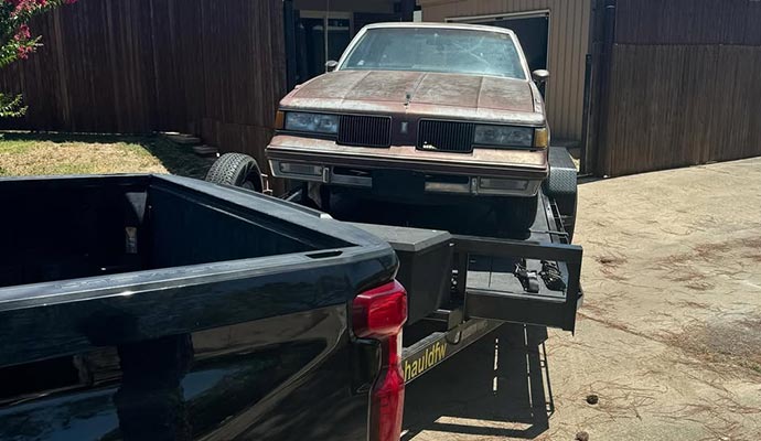 Old rusty sedan car loaded on a black PJ flatbed trailer 