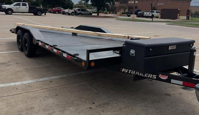 PJ flatbed trailer with toolbox and wooden planks in parking lot