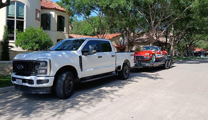 Personal car being transported on a trailer by a white pickup truck