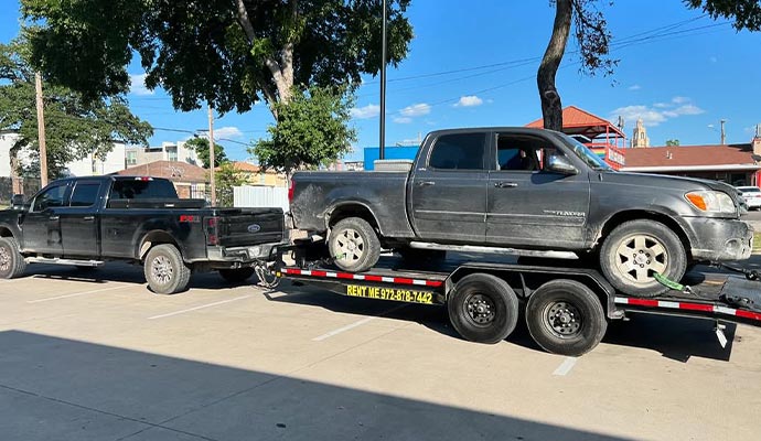 Truck being hauled on a trailer by a white pickup truck