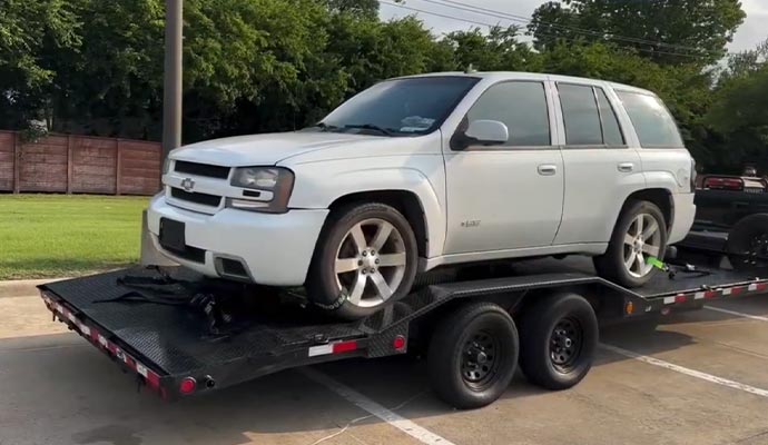 White car being hauled on a trailer on the road