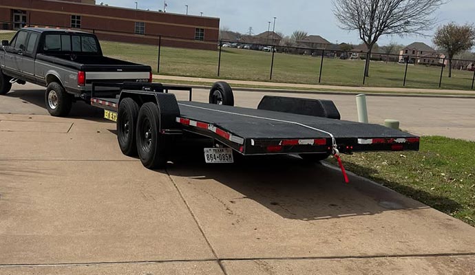 A flatbed car and truck trailer hitched to a pickup truck, ready for rental use in Dallas.