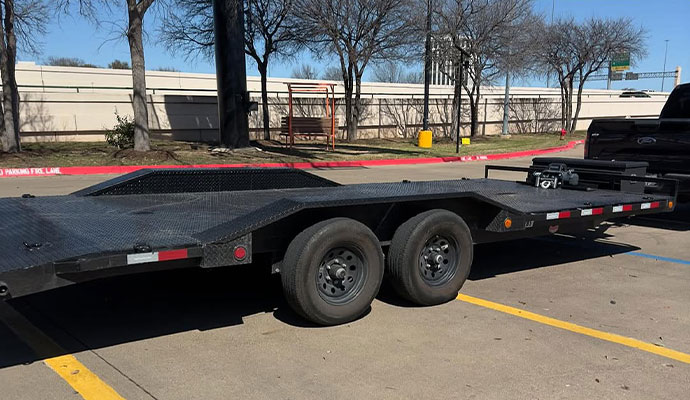 Black car hauler trailer with a flatbed and tandem axles parked in a lot
