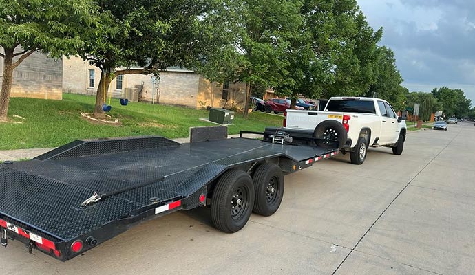 A heavy-duty flatbed trailer hitched to a pickup truck, designed for safe and reliable race car transport.