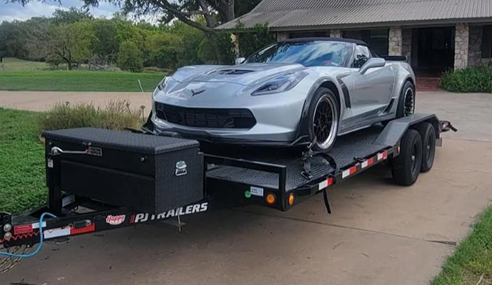 A silver race car securely loaded on a flatbed trailer, ready for transport to a racing event.