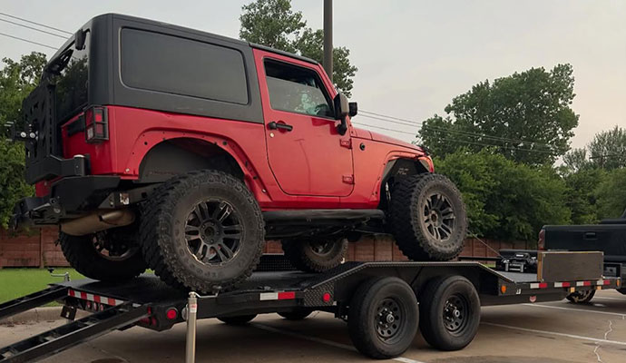 Red Jeep Wrangler loaded onto a flatbed trailer for transport