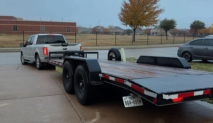 Silver pickup truck hitched to a large black tandem-axle flatbed trailer